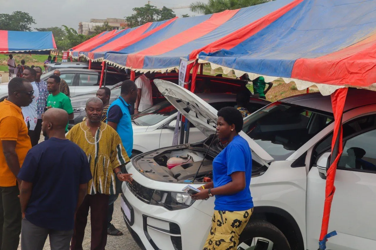 A dealer explaining an electric car to visitors under the exhibition tents