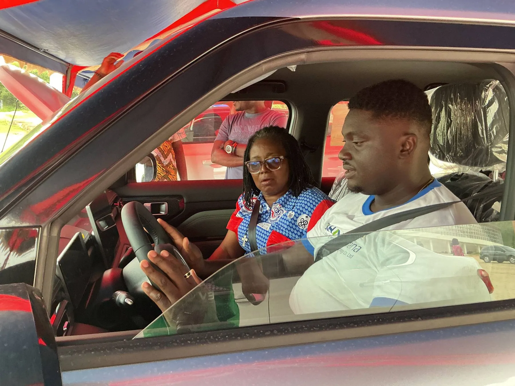 A UEW staff member behind the wheel of an electric car on a test drive, with a GSI team member in the passenger seat