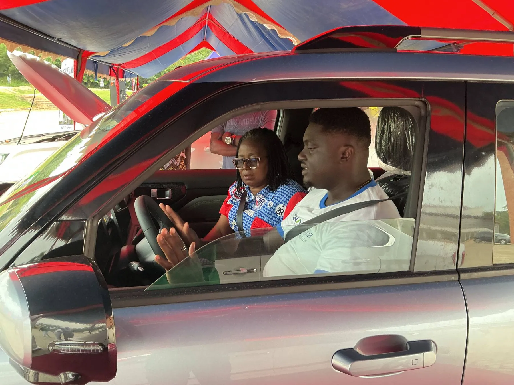 A UEW staff member at the wheel of an electric car during a test drive, with a GSI team member beside her