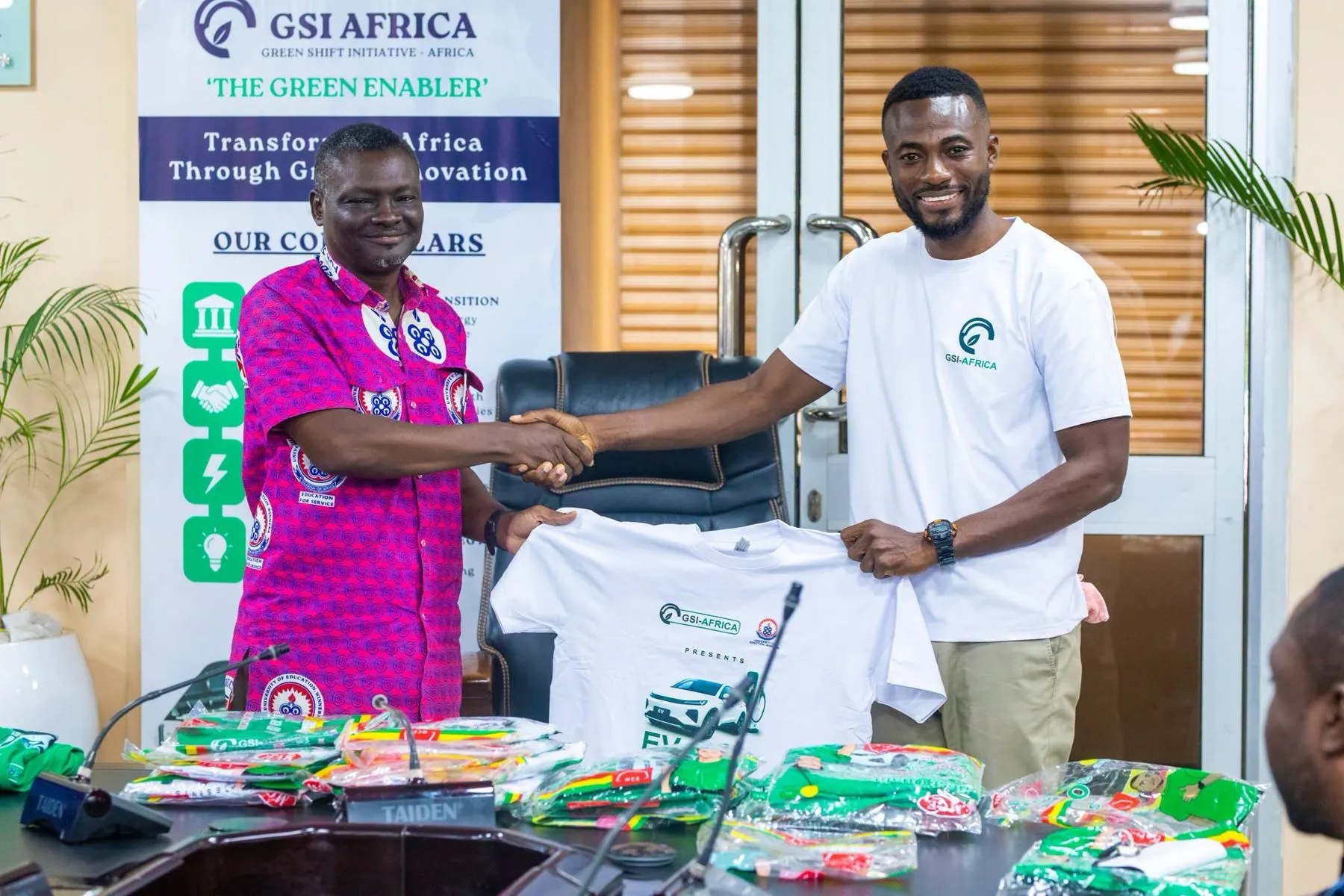 A UEW official and a GSI team member shaking hands while holding a GSI T-shirt