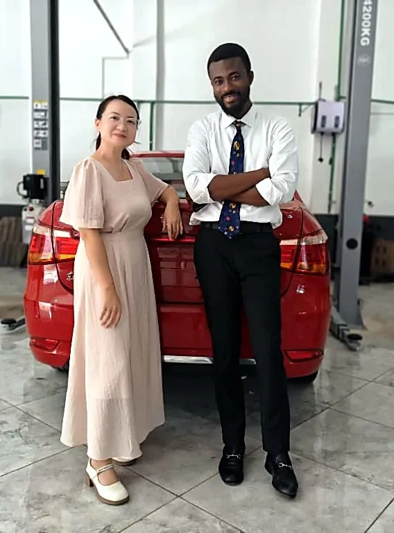 Prince Selorm Mawudzro with a supplier beside a red electric car in a workshop