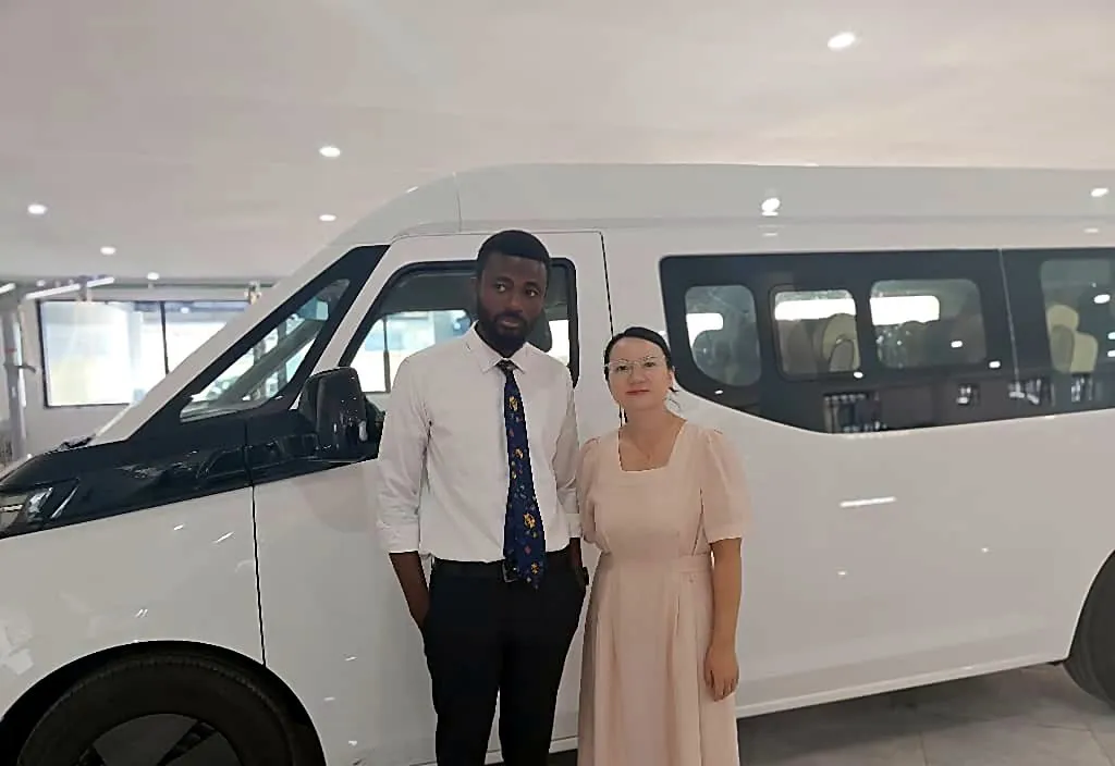 Prince Selorm Mawudzro with a supplier beside a white electric minivan in a showroom